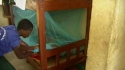 Miteja Sec. School – A student hangs a new net and makes sure it is tucked under the mattress properly.